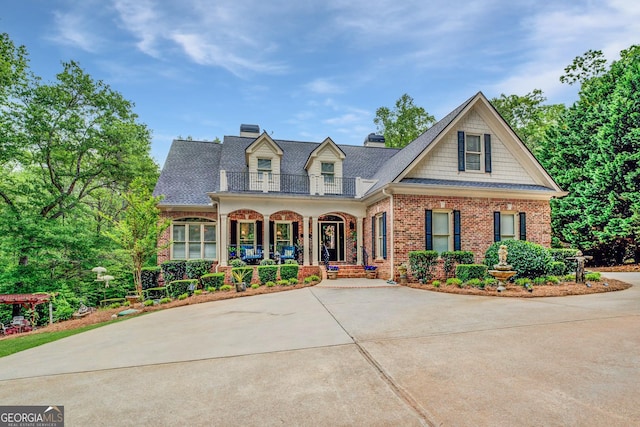 view of front of house featuring a porch, a chimney, brick siding, a balcony, and a shingled roof