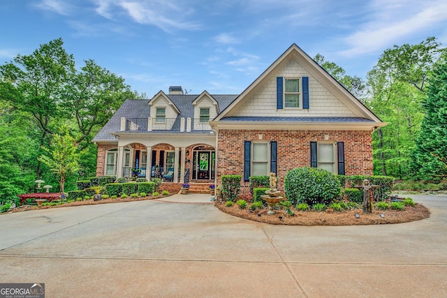 craftsman-style house with a shingled roof, brick siding, a chimney, a balcony, and covered porch