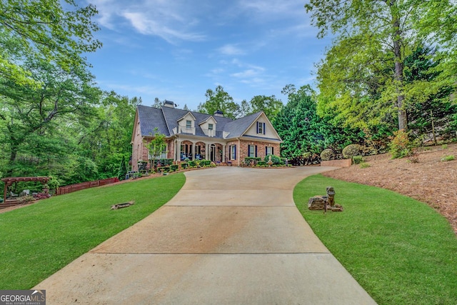 view of front facade with covered porch, a front yard, a chimney, brick siding, and driveway