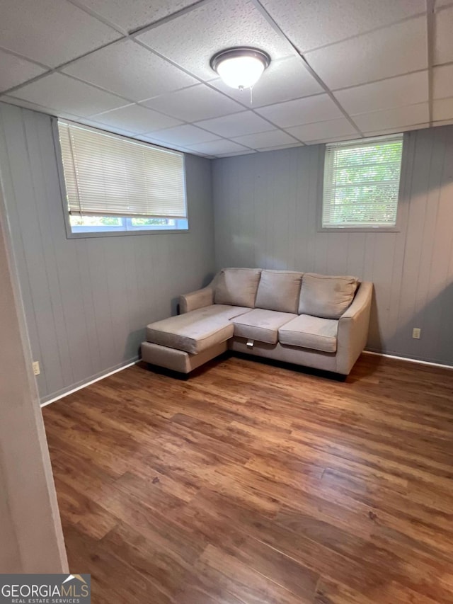 living room with baseboards, wood walls, a drop ceiling, and wood finished floors