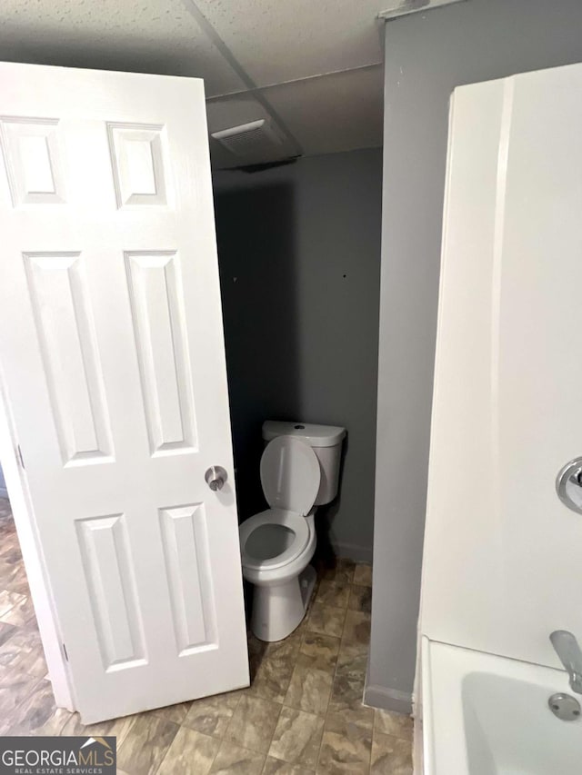 full bathroom featuring toilet and a drop ceiling