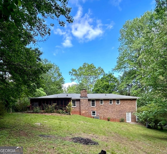 back of house featuring brick siding, a lawn, and a chimney