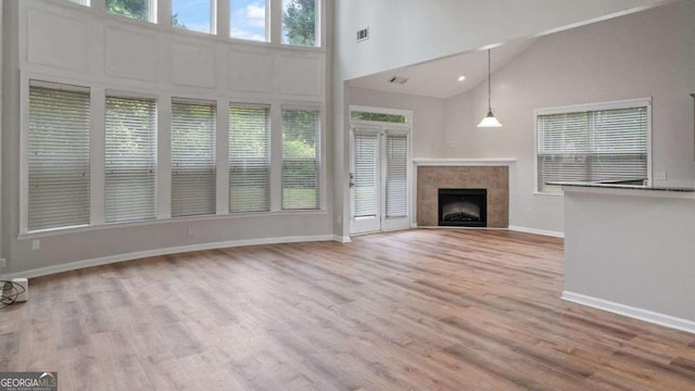 unfurnished living room with visible vents, wood finished floors, a fireplace, baseboards, and high vaulted ceiling