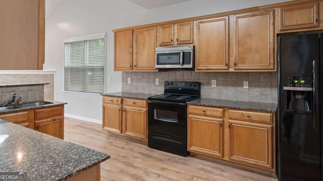 kitchen with a sink, dark stone countertops, decorative backsplash, light wood-type flooring, and black appliances