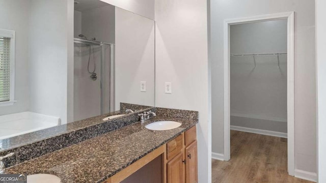 bathroom featuring double vanity, a shower stall, wood finished floors, a sink, and a spacious closet