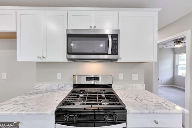 kitchen with gas stove, white cabinets, stainless steel microwave, and light stone countertops