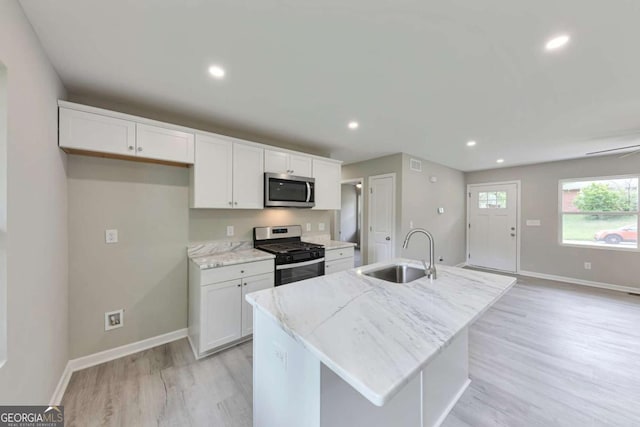 kitchen with baseboards, white cabinets, a sink, light wood finished floors, and stainless steel appliances
