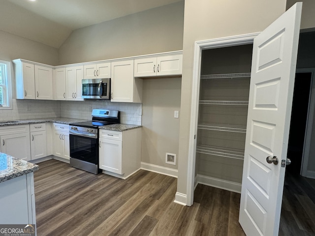kitchen featuring decorative backsplash, appliances with stainless steel finishes, vaulted ceiling, light stone counters, and dark wood-style floors