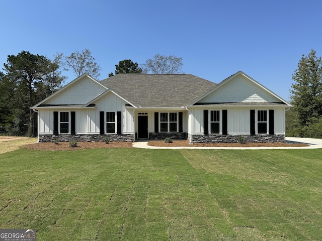 view of front facade featuring a shingled roof, board and batten siding, a front yard, and stone siding