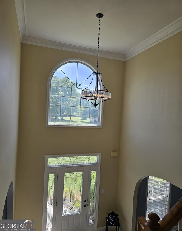 foyer entrance with crown molding, a chandelier, a towering ceiling, and arched walkways