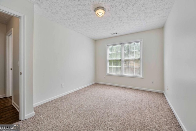 carpeted spare room featuring visible vents, a textured ceiling, and baseboards