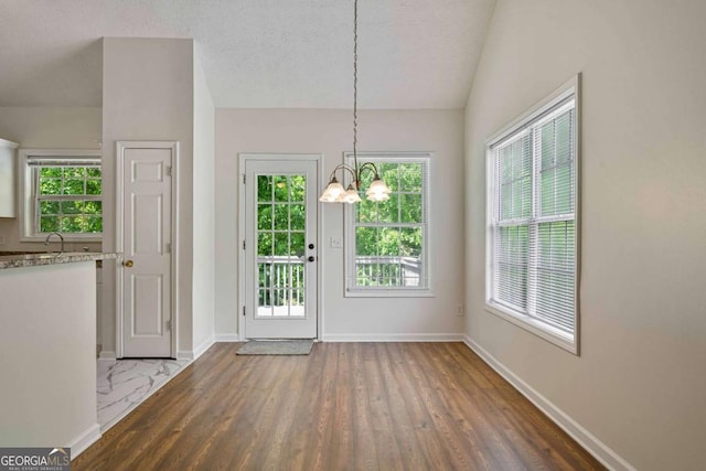 doorway featuring a textured ceiling, vaulted ceiling, wood finished floors, baseboards, and a chandelier