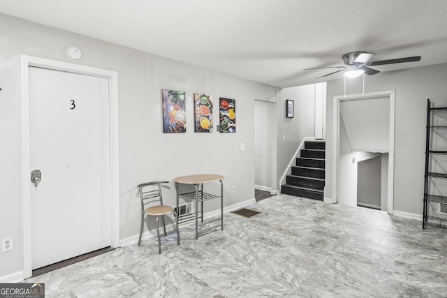 basement featuring baseboards, ceiling fan, stairs, and marble finish floor