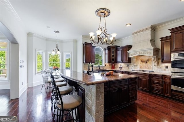 kitchen with a kitchen bar, tasteful backsplash, dark wood finished floors, custom exhaust hood, and stainless steel appliances