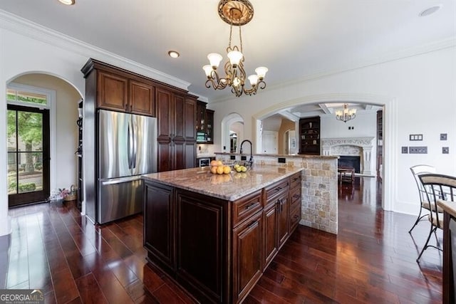 kitchen featuring an inviting chandelier, a fireplace, light stone counters, stainless steel fridge, and ornamental molding
