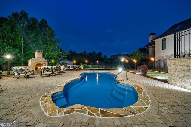 pool at twilight featuring a patio, a lit fireplace, fence, and a fenced in pool