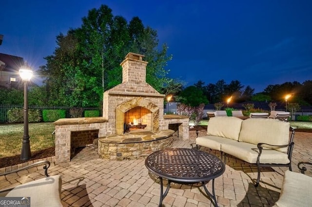 patio at night with fence and an outdoor living space with a fireplace