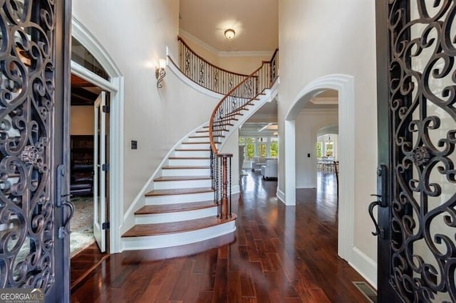 entryway with crown molding, stairs, wood finished floors, baseboards, and arched walkways