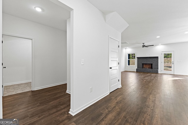 unfurnished living room with baseboards, ceiling fan, a brick fireplace, and dark wood-type flooring