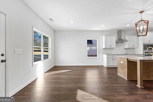 kitchen with visible vents, dark wood-type flooring, wall chimney exhaust hood, stainless steel microwave, and a chandelier