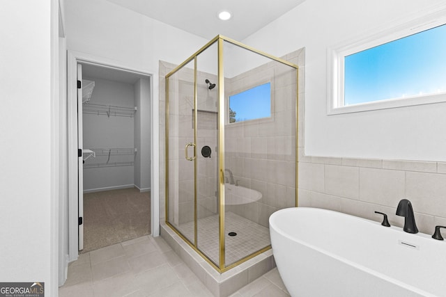 bathroom with tile patterned flooring, a freestanding bath, a spacious closet, and a shower stall