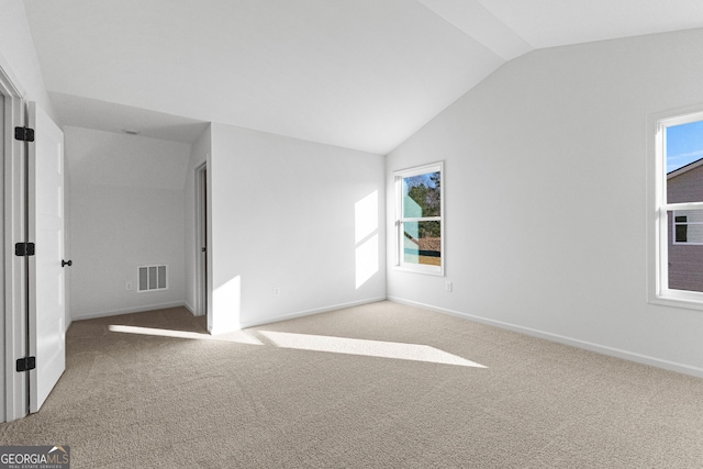 empty room featuring carpet floors, baseboards, vaulted ceiling, and visible vents