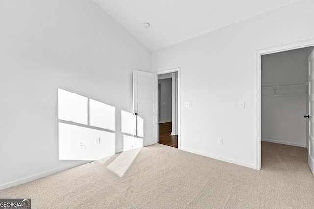 unfurnished bedroom featuring baseboards, carpet, a spacious closet, and vaulted ceiling