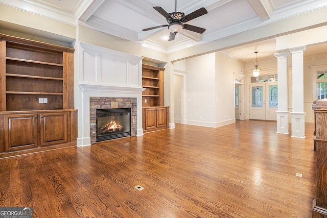unfurnished living room featuring ceiling fan, a stone fireplace, wood finished floors, ornamental molding, and coffered ceiling