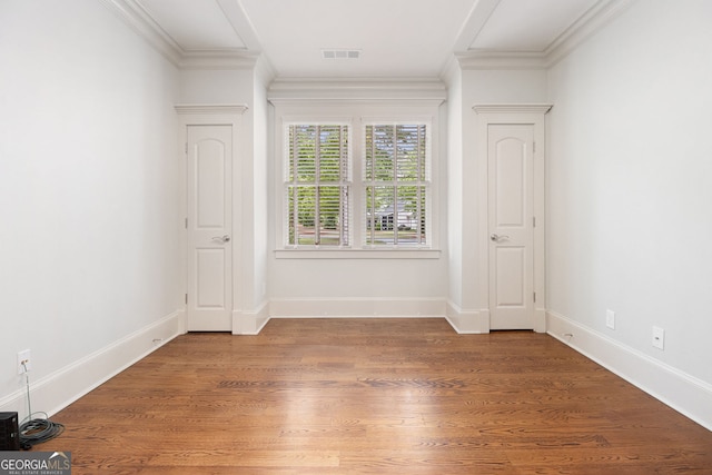 interior space with baseboards, ornamental molding, wood finished floors, and visible vents