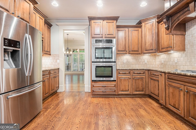 kitchen featuring brown cabinetry, crown molding, tasteful backsplash, light stone countertops, and stainless steel appliances
