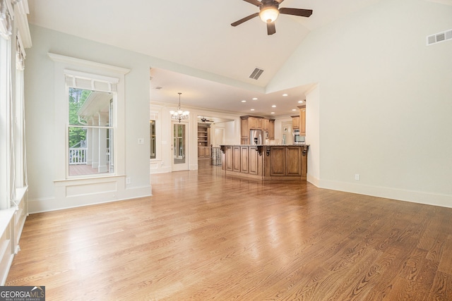 unfurnished living room featuring visible vents, ceiling fan with notable chandelier, vaulted ceiling, and light wood-type flooring