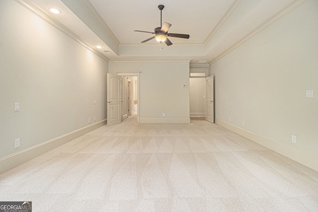 empty room with crown molding, a ceiling fan, a raised ceiling, and light carpet