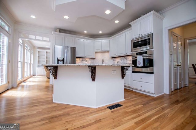 213 Shady Valley Dr, Carrollton, GA 30116 - kitchen featuring appliances with stainless steel finishes, ornamental molding, a breakfast bar area, white cabinets, and light wood-style flooring