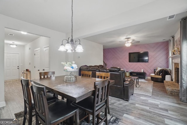 11028 Southwood Dr, Hampton, GA 30228 - dining room with a fireplace, an accent wall, ceiling fan with notable chandelier, light wood-type flooring, and visible vents