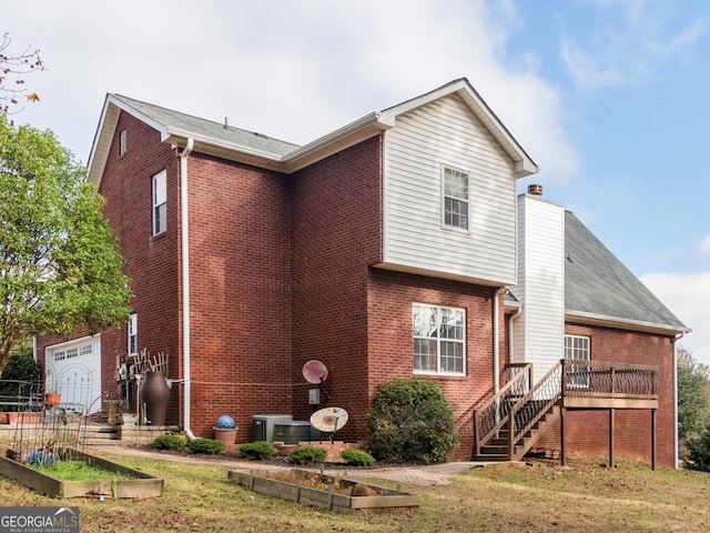 exterior space with a wooden deck, a vegetable garden, brick siding, central AC unit, and stairway