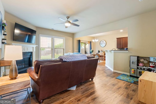 living area featuring visible vents, wood finished floors, baseboards, ceiling fan with notable chandelier, and a glass covered fireplace