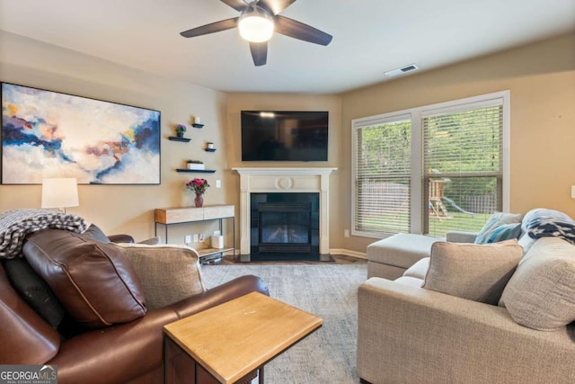 living room featuring ceiling fan, visible vents, a fireplace with flush hearth, and baseboards