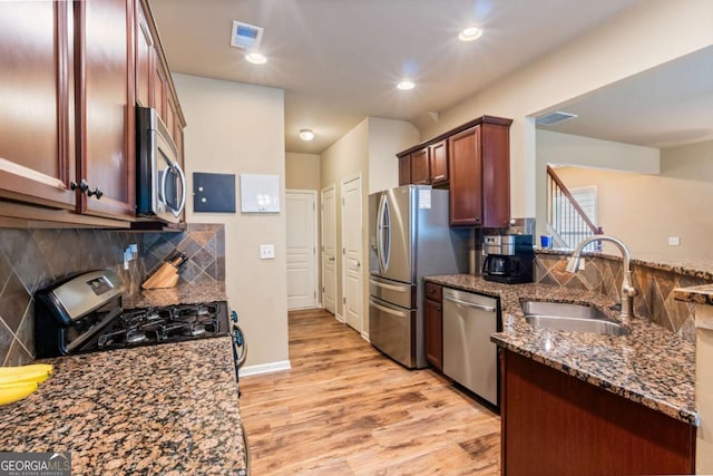 kitchen with visible vents, light wood-type flooring, a sink, dark stone countertops, and stainless steel appliances