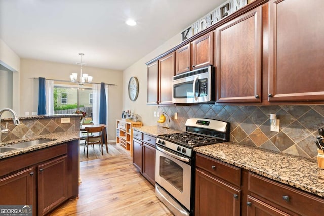 kitchen with an inviting chandelier, backsplash, a sink, light wood-style floors, and stainless steel appliances