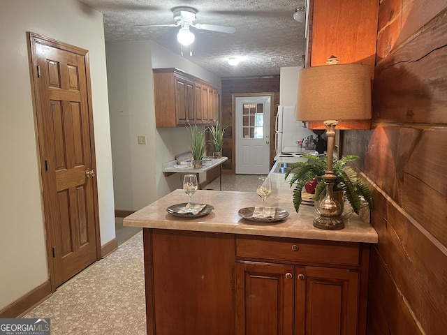 kitchen featuring a ceiling fan, brown cabinets, light countertops, baseboards, and freestanding refrigerator