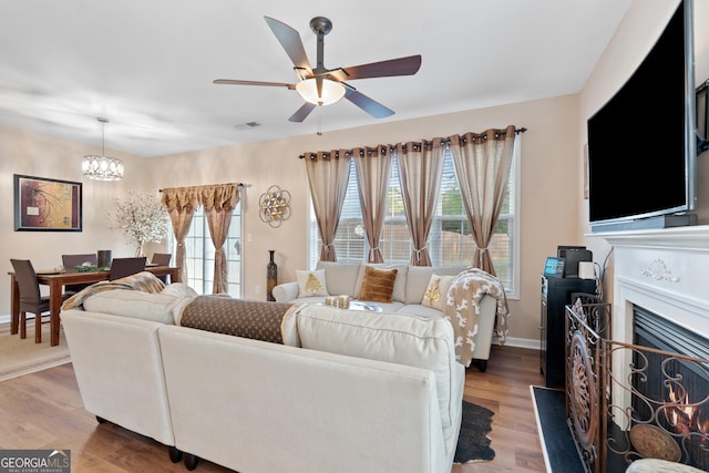 living area with baseboards, light wood-style flooring, ceiling fan with notable chandelier, and a fireplace