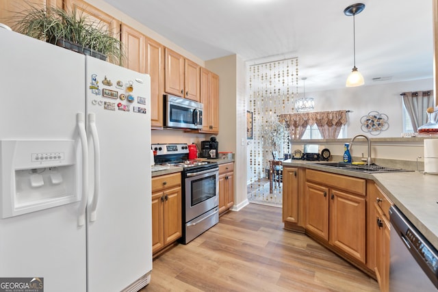 kitchen with appliances with stainless steel finishes, a sink, light wood-style floors, plenty of natural light, and pendant lighting