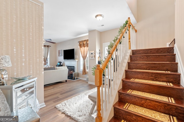 stairway with baseboards, wood finished floors, and a warm lit fireplace