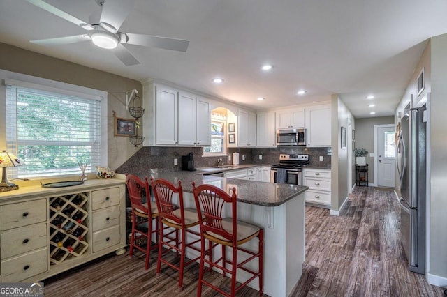kitchen with appliances with stainless steel finishes, a peninsula, dark wood-type flooring, backsplash, and visible vents