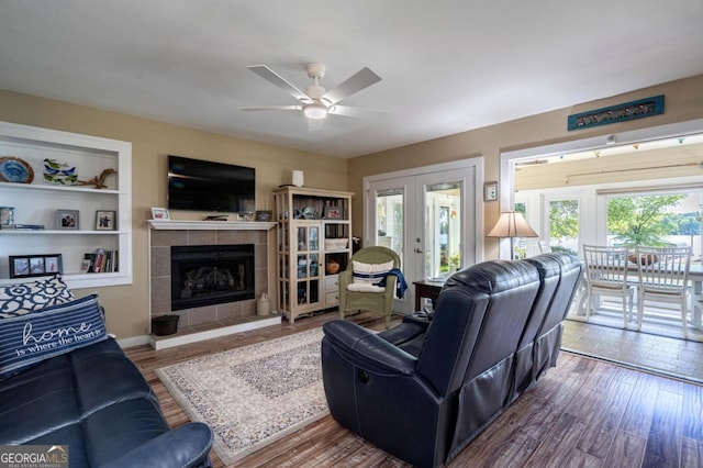 living room featuring a ceiling fan, french doors, a tiled fireplace, and wood finished floors