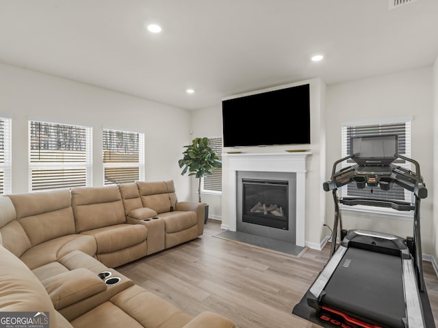 living area with recessed lighting, baseboards, light wood-type flooring, and a fireplace with flush hearth