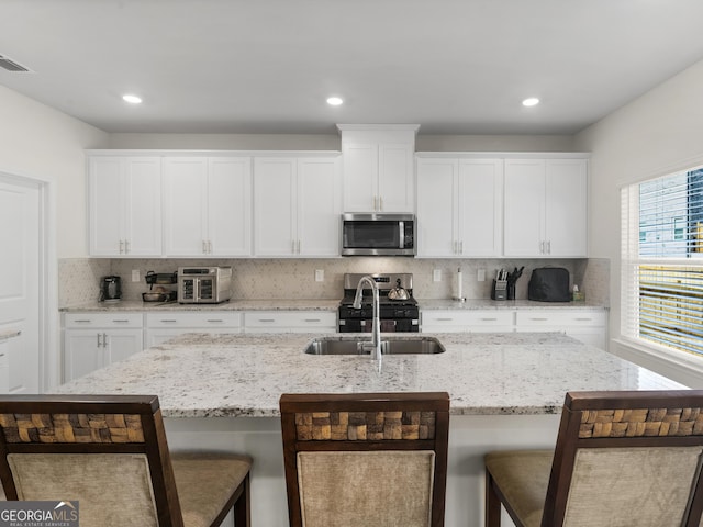 kitchen with a sink, a breakfast bar area, stainless steel microwave, decorative backsplash, and gas range oven
