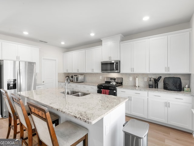kitchen with backsplash, a kitchen bar, visible vents, appliances with stainless steel finishes, and a sink