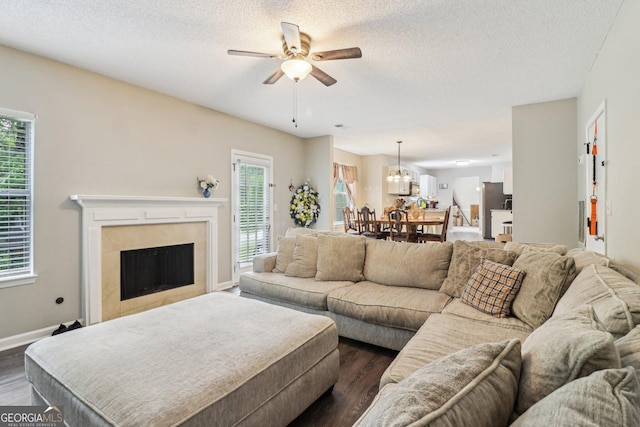 4015 Soaring Dr, Douglasville, GA 30135 - living room featuring a textured ceiling, a tiled fireplace, baseboards, ceiling fan with notable chandelier, and dark wood-type flooring