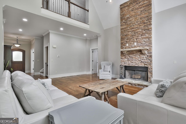 living room featuring crown molding, a fireplace, baseboards, wood finished floors, and a towering ceiling